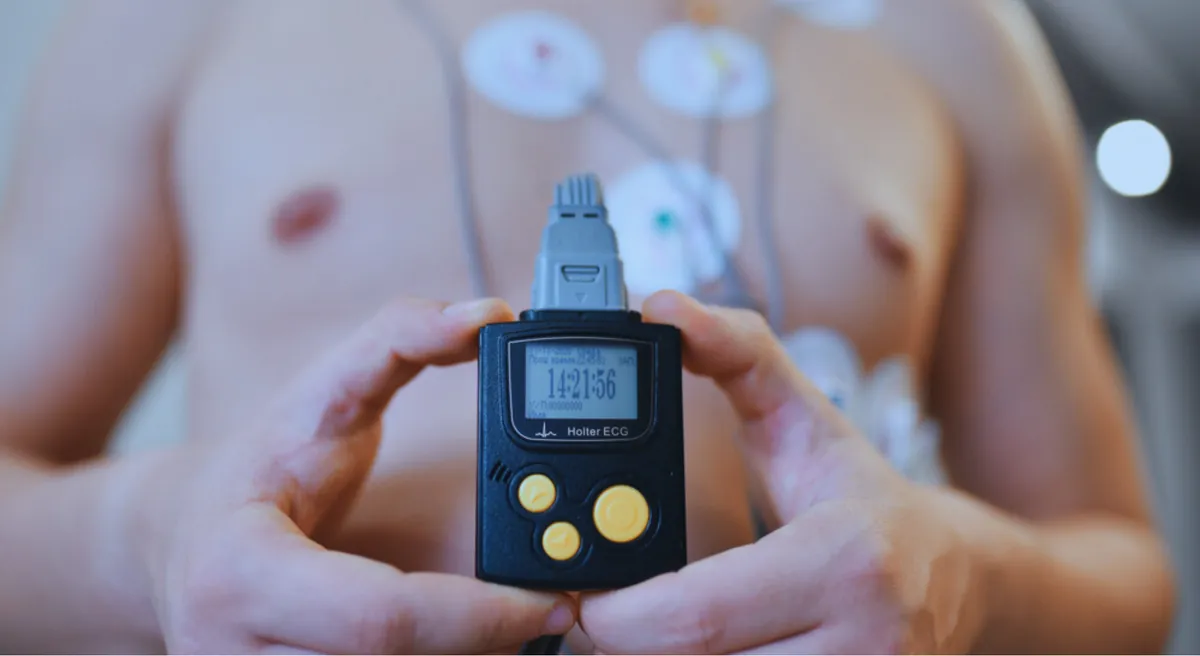 Monitor Holter sostenido en las manos, con los electrodos colocados en el pecho del paciente